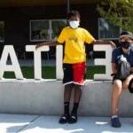 Two students stand together outside wearing masks in front of a school