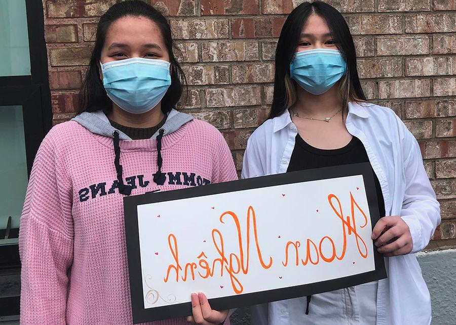 Two students in masks hold a sign that says welcome in vietnamese