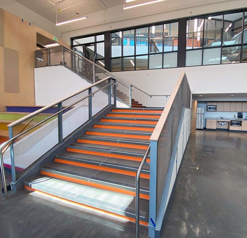 an interior stair leads up from a concrete floor past a group of windows. 楼梯旁边有一个滑梯