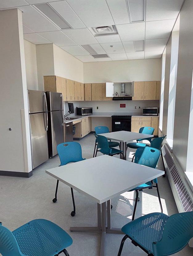 a room with two refrigerators, cabinetry, a stove, two microwaves, and some tables and chairs